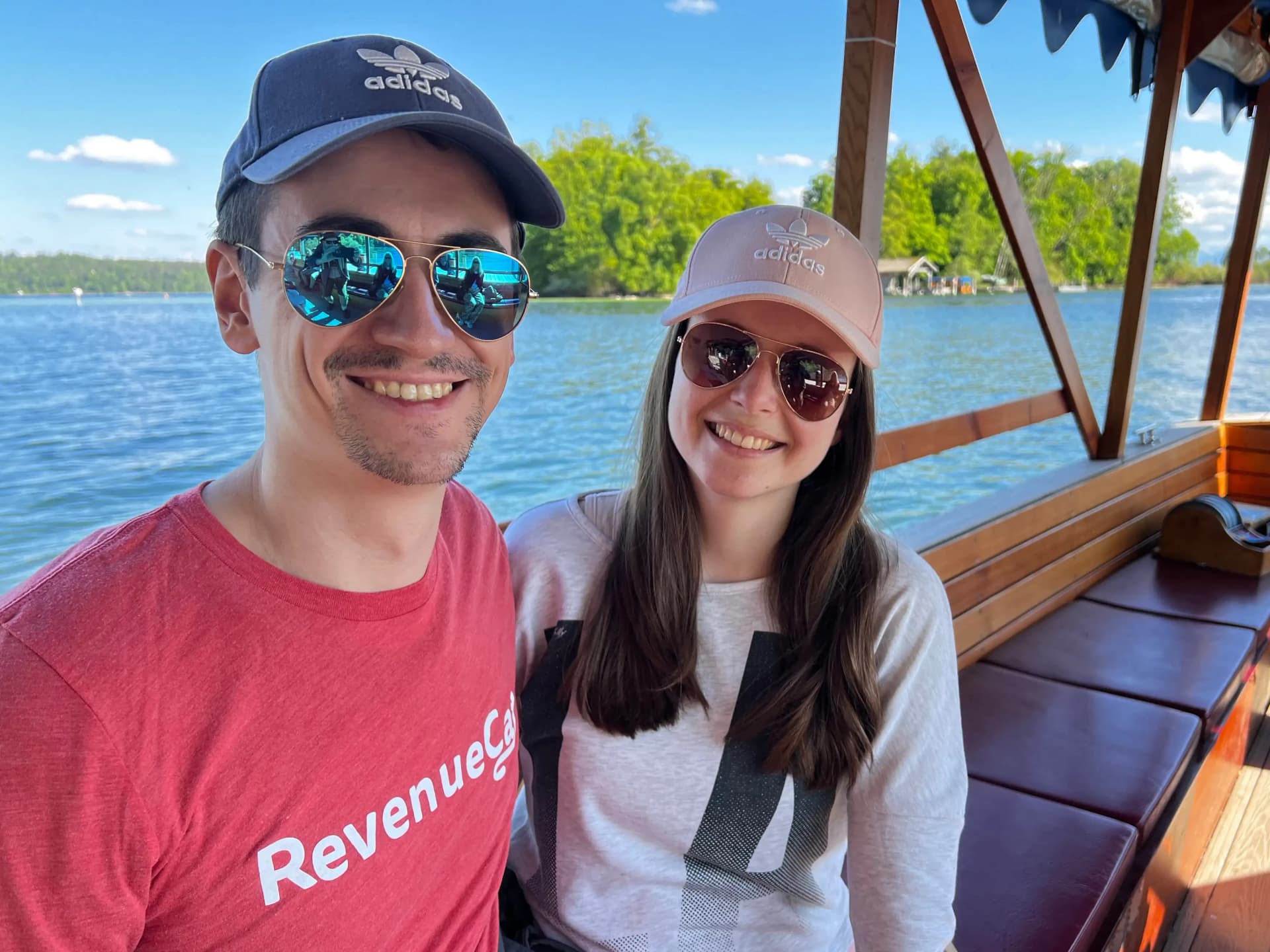 Damjan and Sara on a wooden boat on a Bavarian lake, both wearing Adidas caps